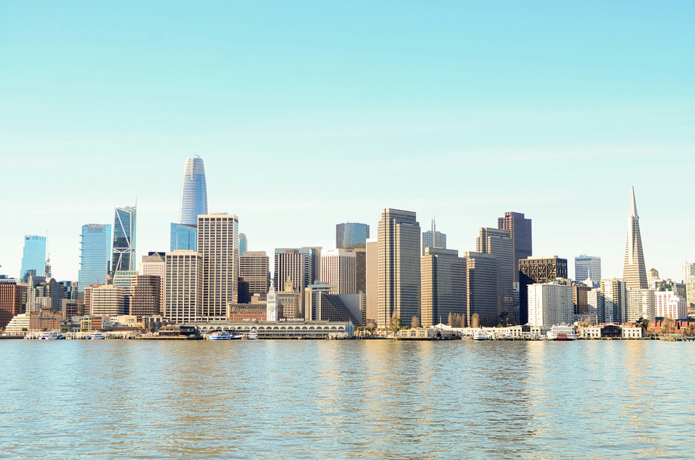 San Francisco skyline viewed across the bay under a clear blue sky, with the Salesforce Tower and Transamerica Pyramid among the cluster of downtown high-rises and the Ferry Building along the waterfront