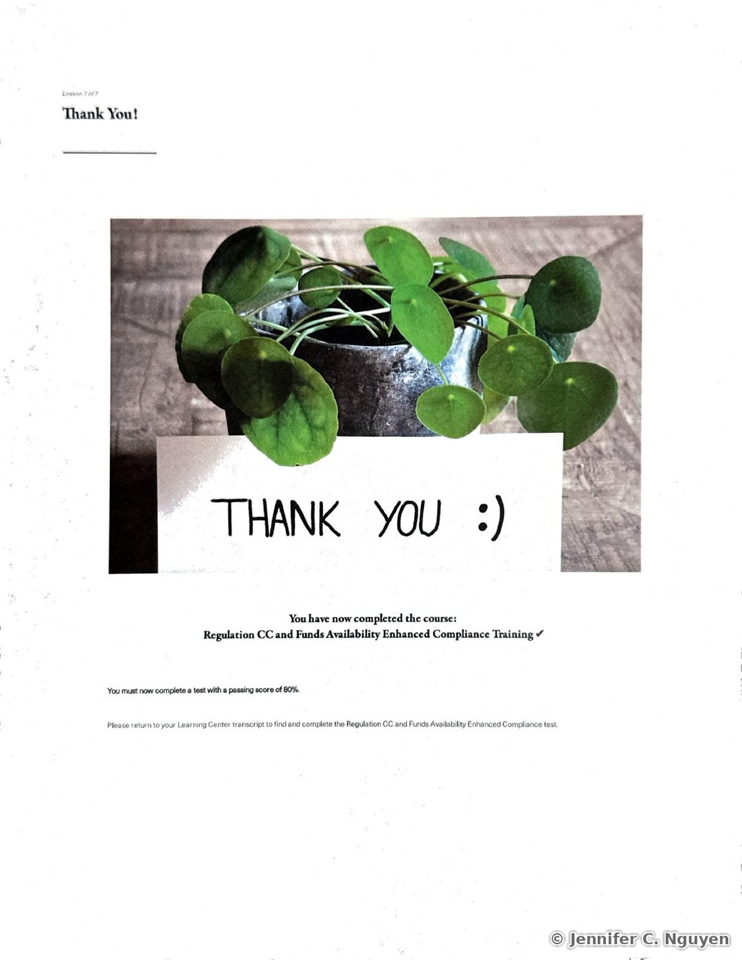 Thank You completion slide with a photo of a potted Chinese money plant on a wood table beside a handwritten Thank You smiley note, confirming completion of the Regulation CC and Funds Availability Enhanced Compliance Training course and instructing the learner to return to their Learning Center transcript to complete the required test with a passing score of 80 percent