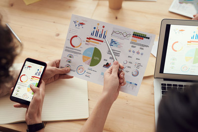 Hands reviewing printed analytics charts and dashboards alongside a phone and laptop